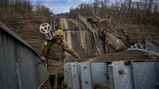 Украинский военнослужащий идет по руинам моста на окраине Бахмута с пустой кассетной гильзой от ракеты "Ураган".